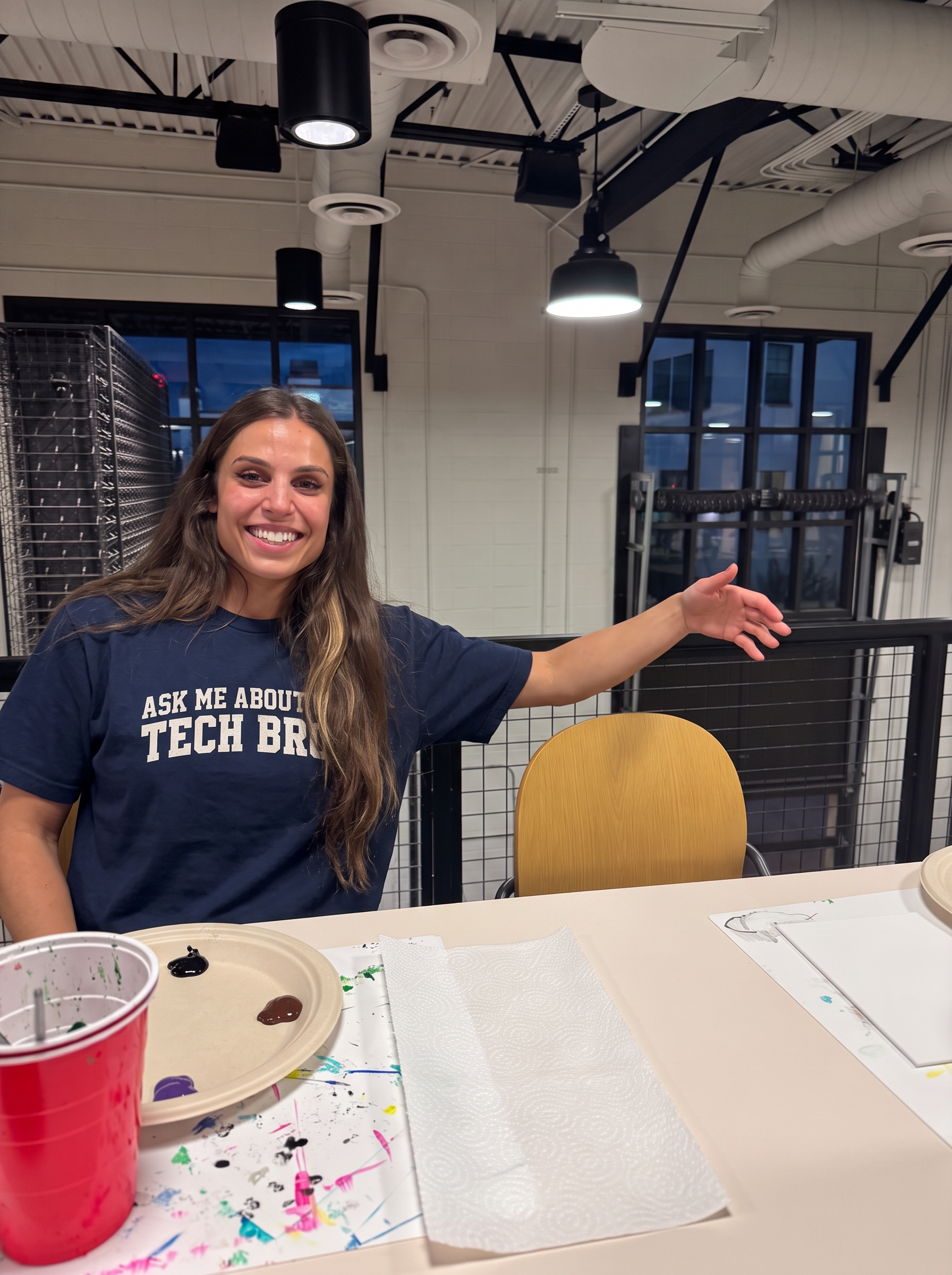 Jasmine Kay smiling at a paint-night table in a navy ASK ME ABOUT MY TECH BROS tee